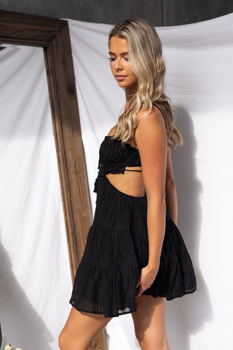 Adjustable black Spirited Dress with elastic neckline, tie details, and a flowy fit, worn by a model against a minimalist background.