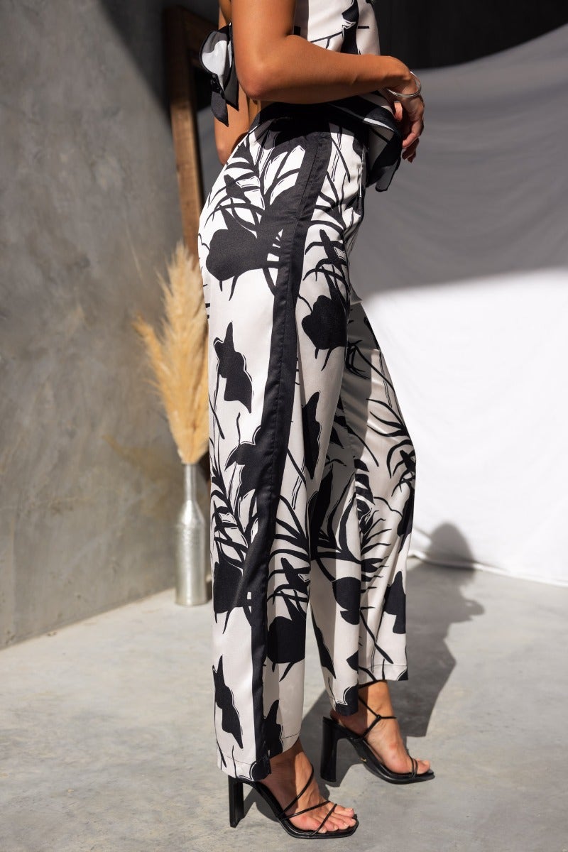 Side view of Persia Pants featuring a floral print, elastic waistband, and pockets, styled with strappy heels.
