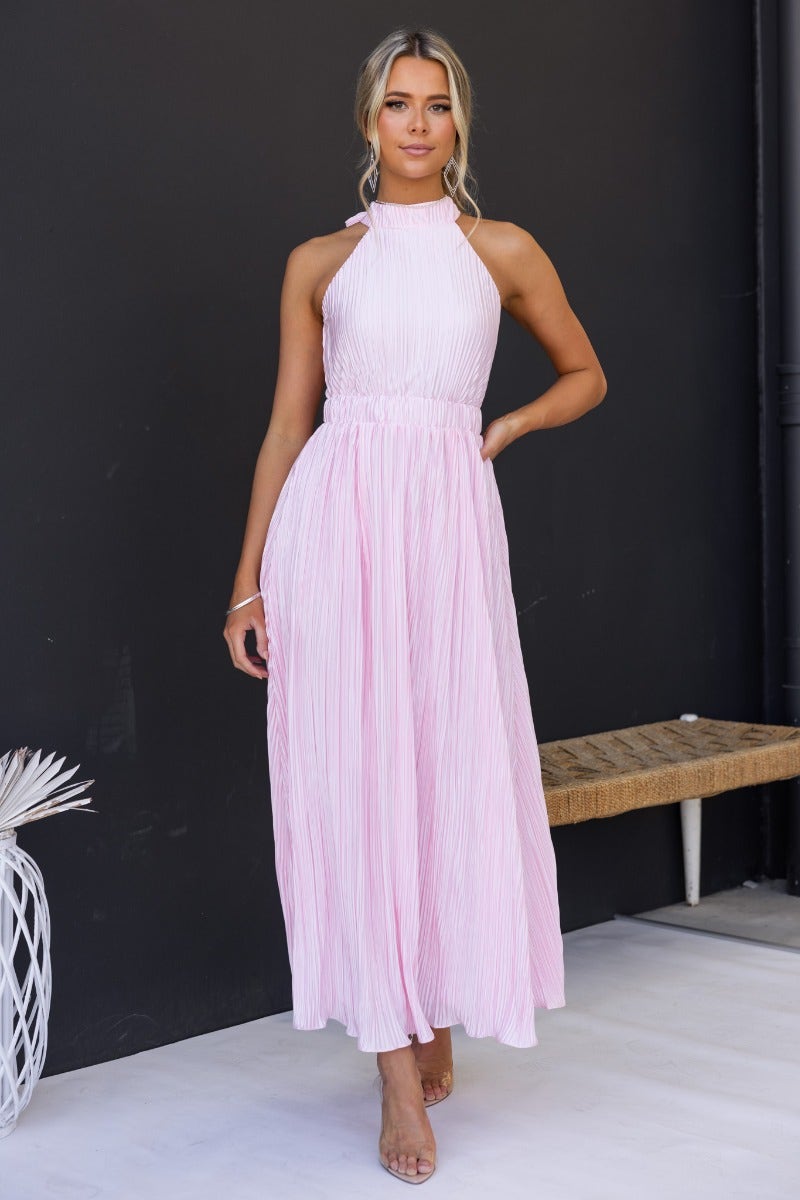 Model wearing Tyran Maxi Dress in pink with pleats and high tie neckline, showcasing elegant summer fashion.