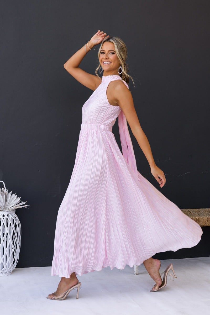 Model in a pink accordion pleat maxi dress showcasing high tie neckline and elastic waistband, exuding elegance.