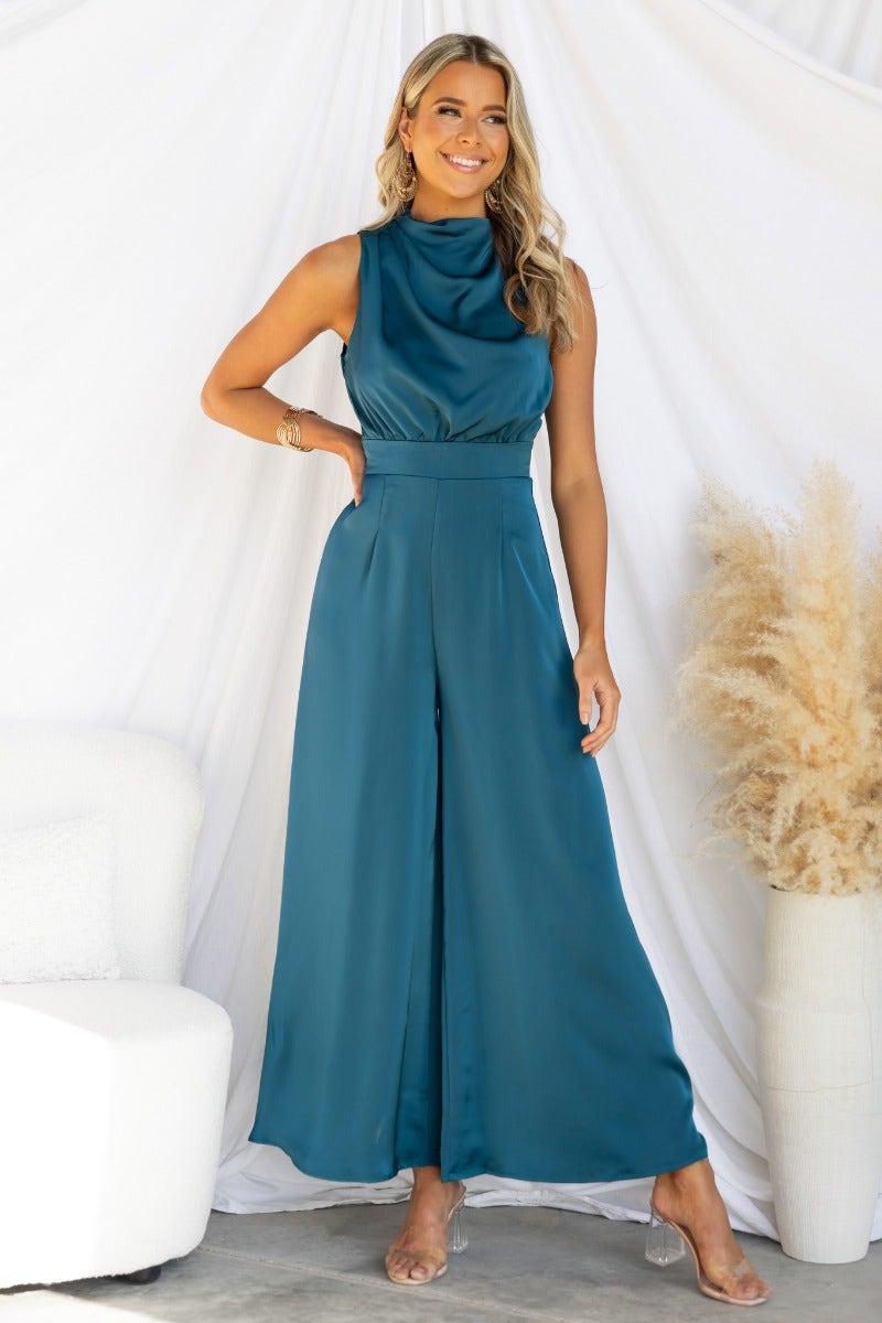 Elyssa satin jumpsuit featuring a high neckline, wide legs, and tie at back, model wearing in teal color.