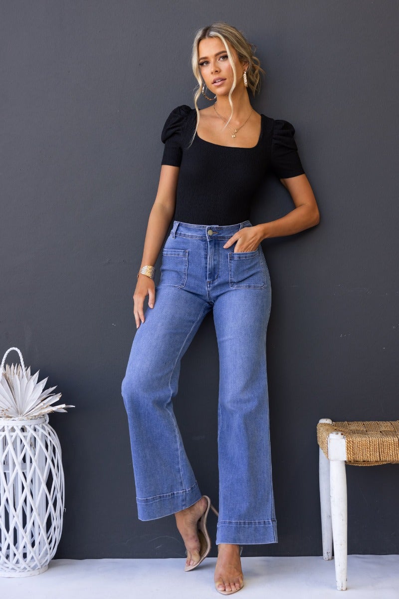 Model wearing Lane Jeans, mid-high waist denim with front and back pockets, styled with a black top.