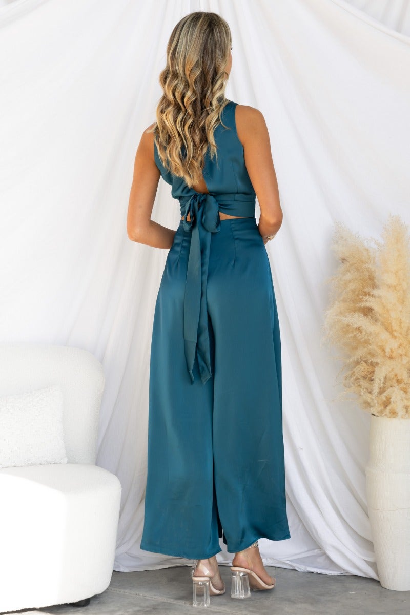 Back view of Elyssa Satin Jumpsuit featuring a high neckline, tie-back detail, and wide legs in teal color.