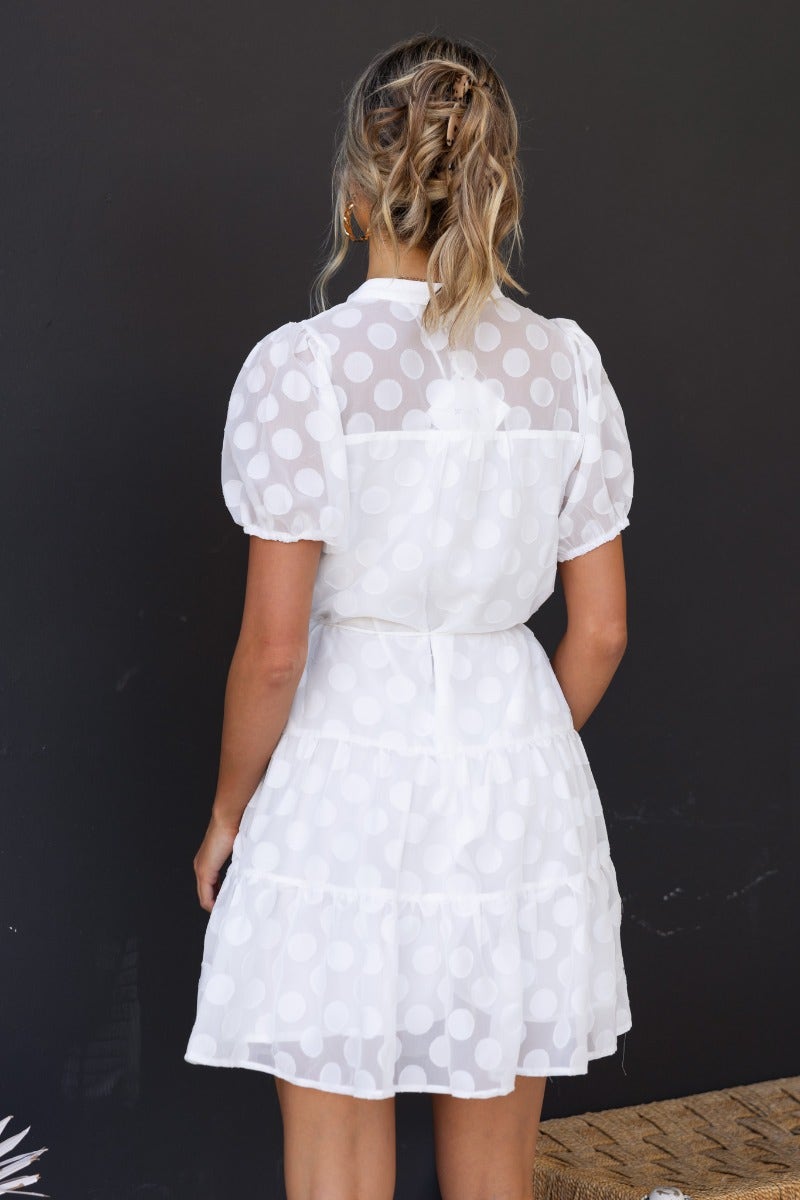 Back view of Leylah Dress featuring textured polka dot fabric, button-up front, and elastic sleeve cuffs.