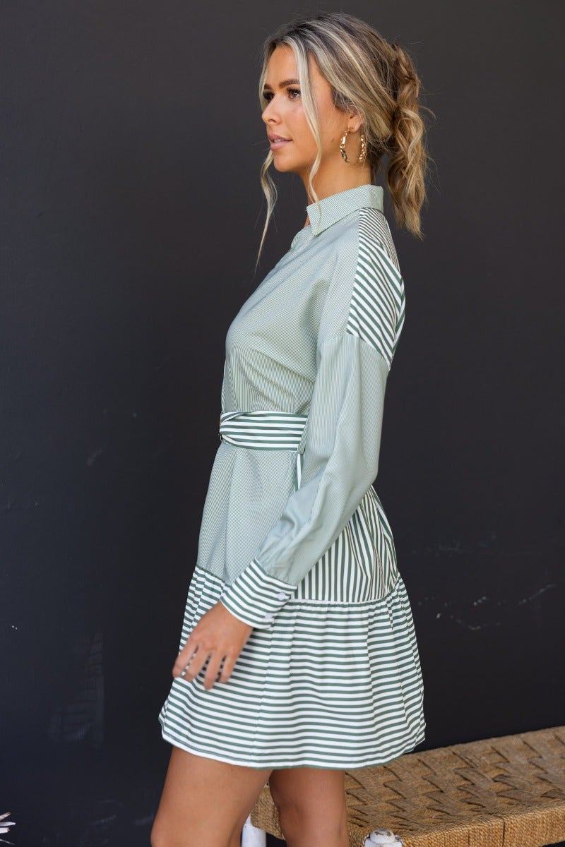 Side view of a model wearing a light green stripe Tiller Dress with a collar, button-up front, and removable belt.