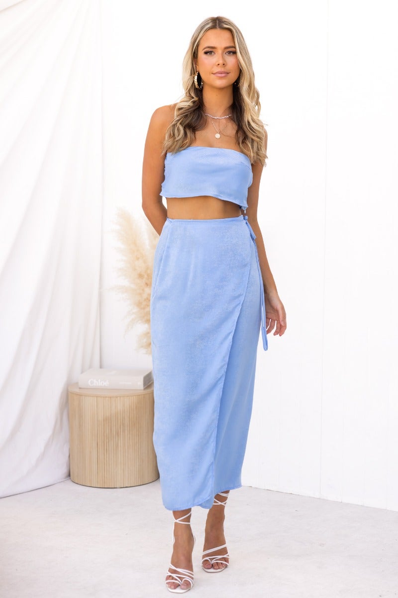 Model wearing a blue Nerida wrap midi skirt with an asymmetric hem and fabric tie, styled with a cropped top.