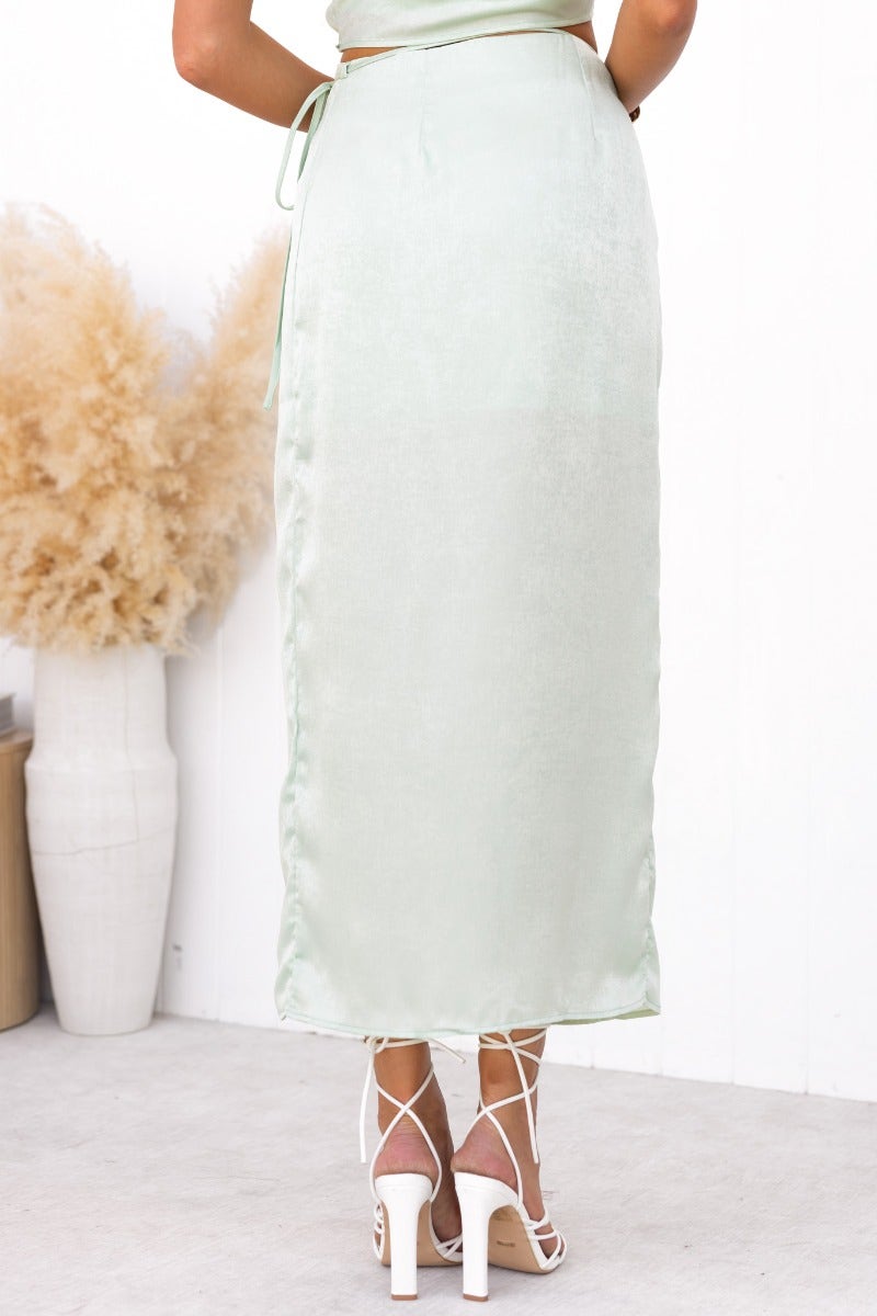 Back view of the Nerida Wrap Midi Skirt in mint green, showcasing the asymmetric hem and fabric tie detail.
