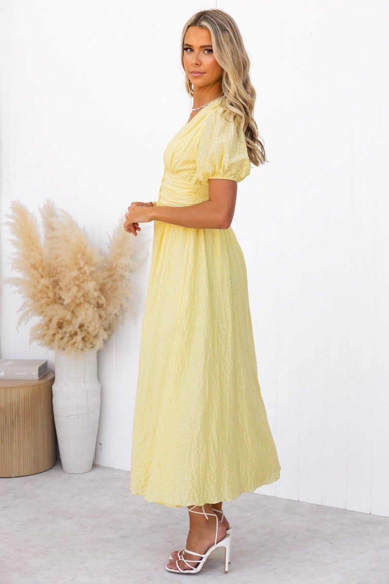 Hollie Maxi Dress in textured yellow fabric, featuring a V-neckline and elastic sleeves, styled with strappy heels.