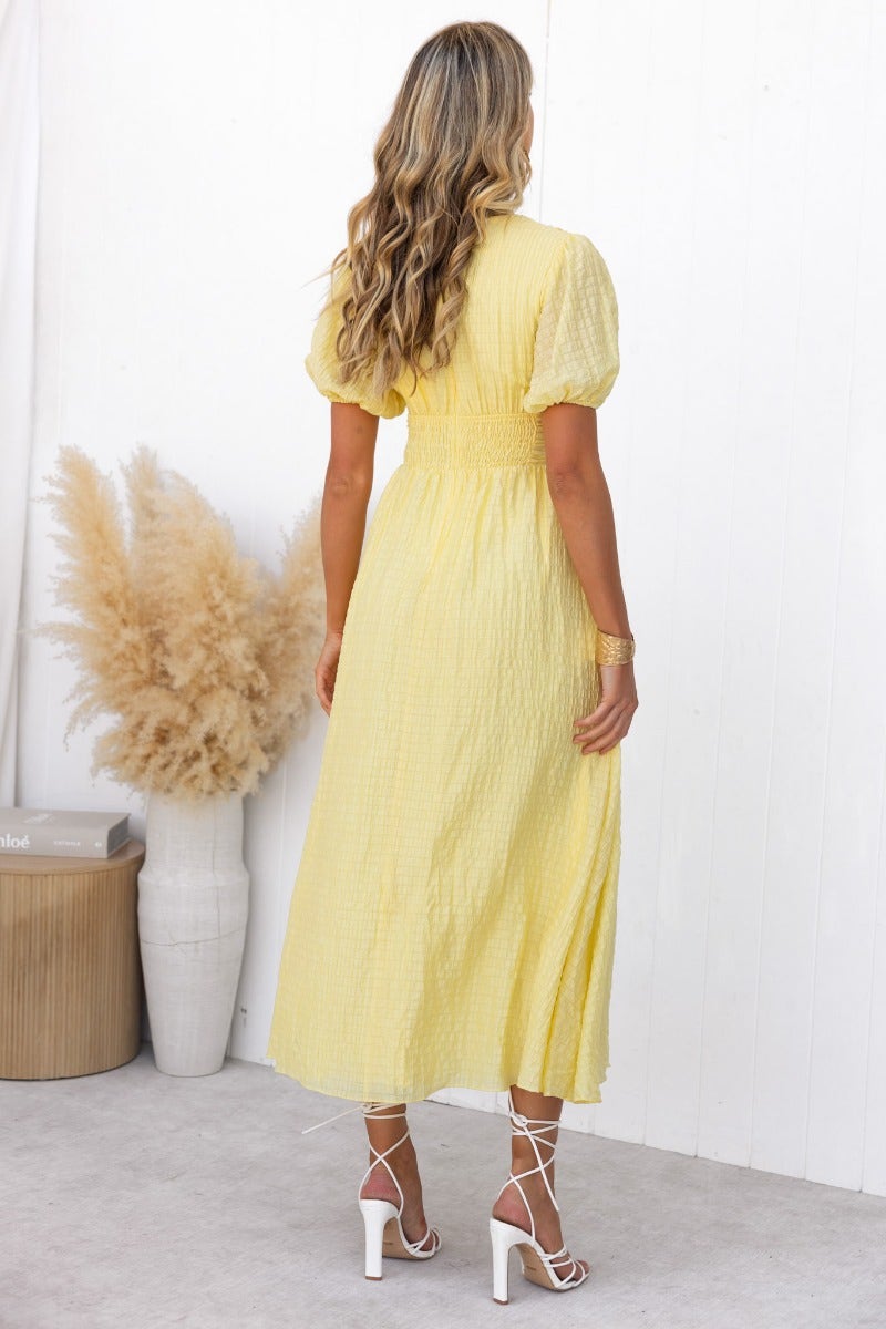 Model showcasing the back of a yellow textured Hollie Maxi Dress with puff sleeves and a flowy design.