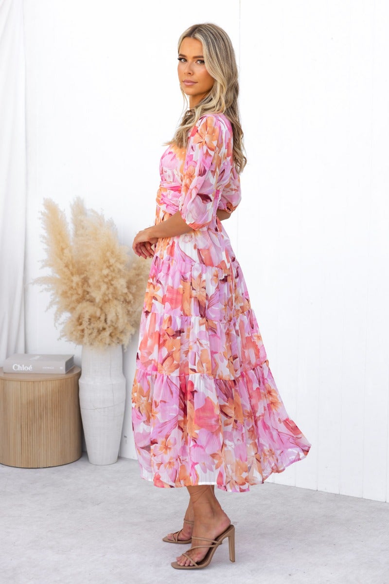Model wearing a floral print Orchi midi dress with a V-neckline and elastic sleeves, showcasing a stylish summer look.