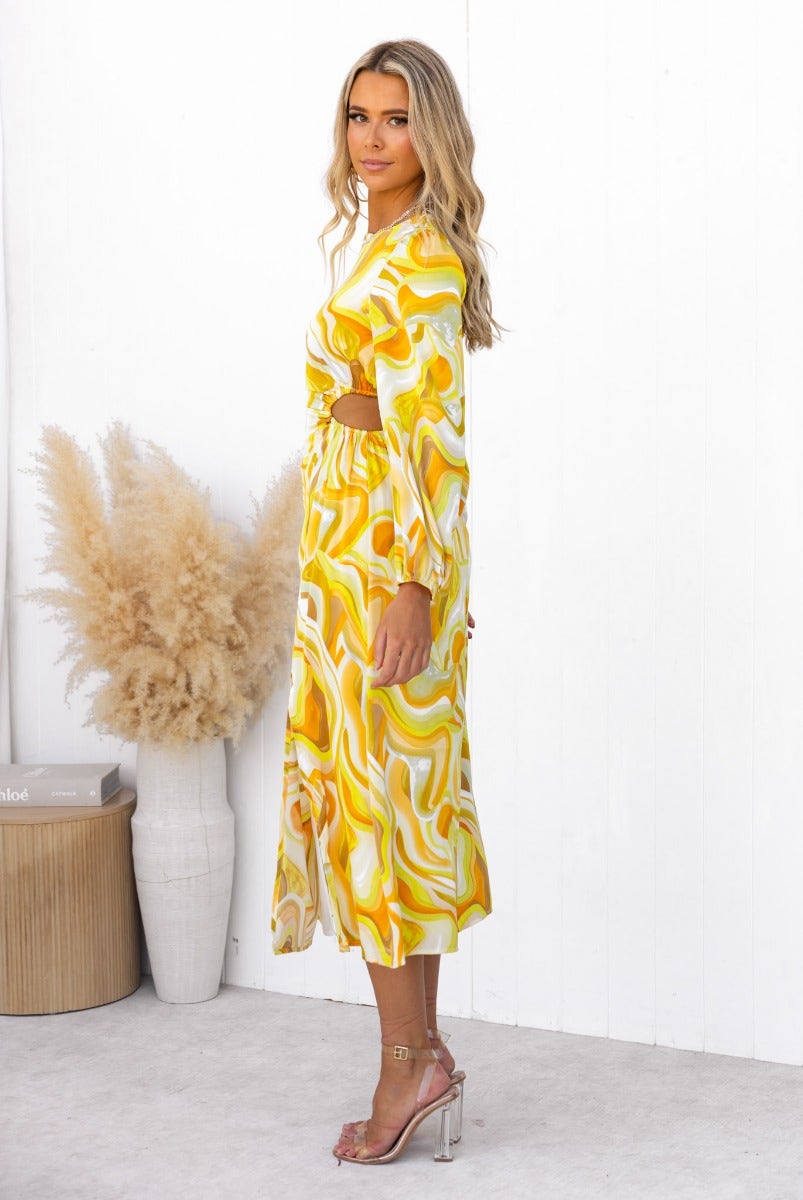 Model wearing a yellow satin Sapphira midi dress with elastic sleeves and cut-outs, styled with transparent heels.