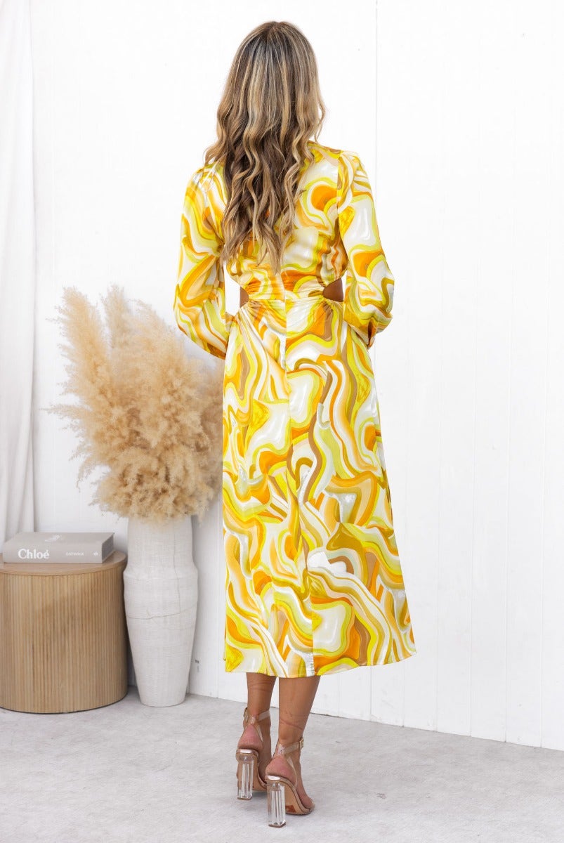 Back view of a woman wearing a colorful yellow and white abstract printed midi dress with long sleeves.