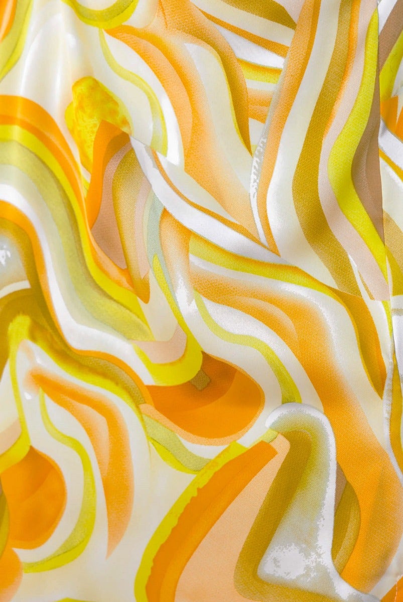 Close-up of vibrant satin fabric featuring fluid waves in yellow, orange, and green tones.