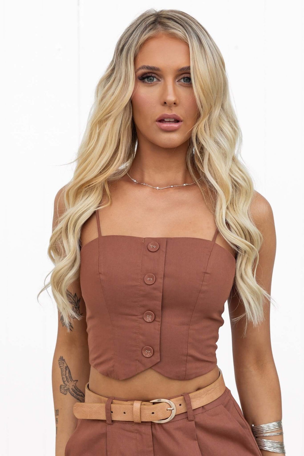 Model wearing the Downtown Top, featuring adjustable spaghetti straps and a button front in a chic brown color.