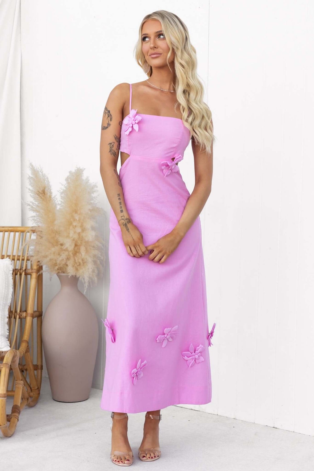 Model wearing a pink Flower Pop Midi Dress with removable flowers and cut out sides, set against a minimal backdrop.