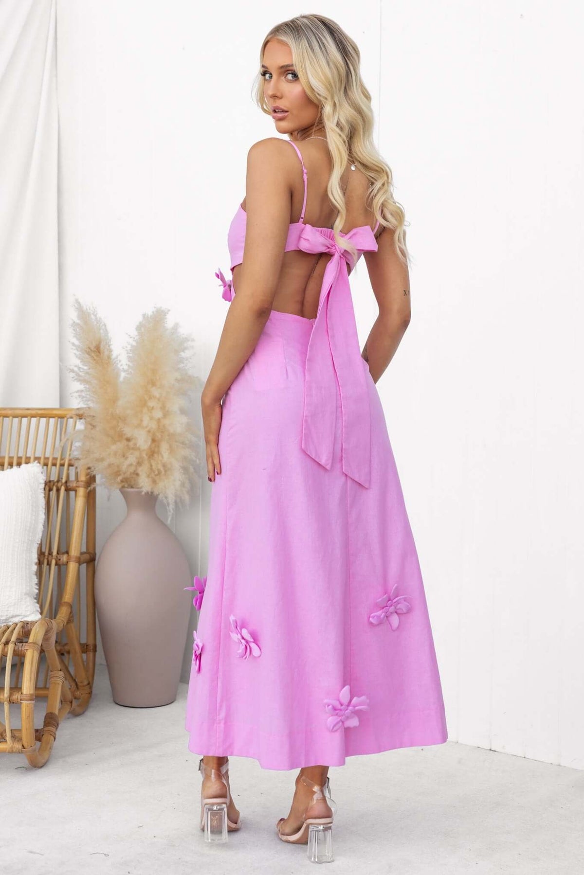 Model wearing a pink Flower Pop Midi Dress with adjustable straps and removable flowers, styled with a boho background.