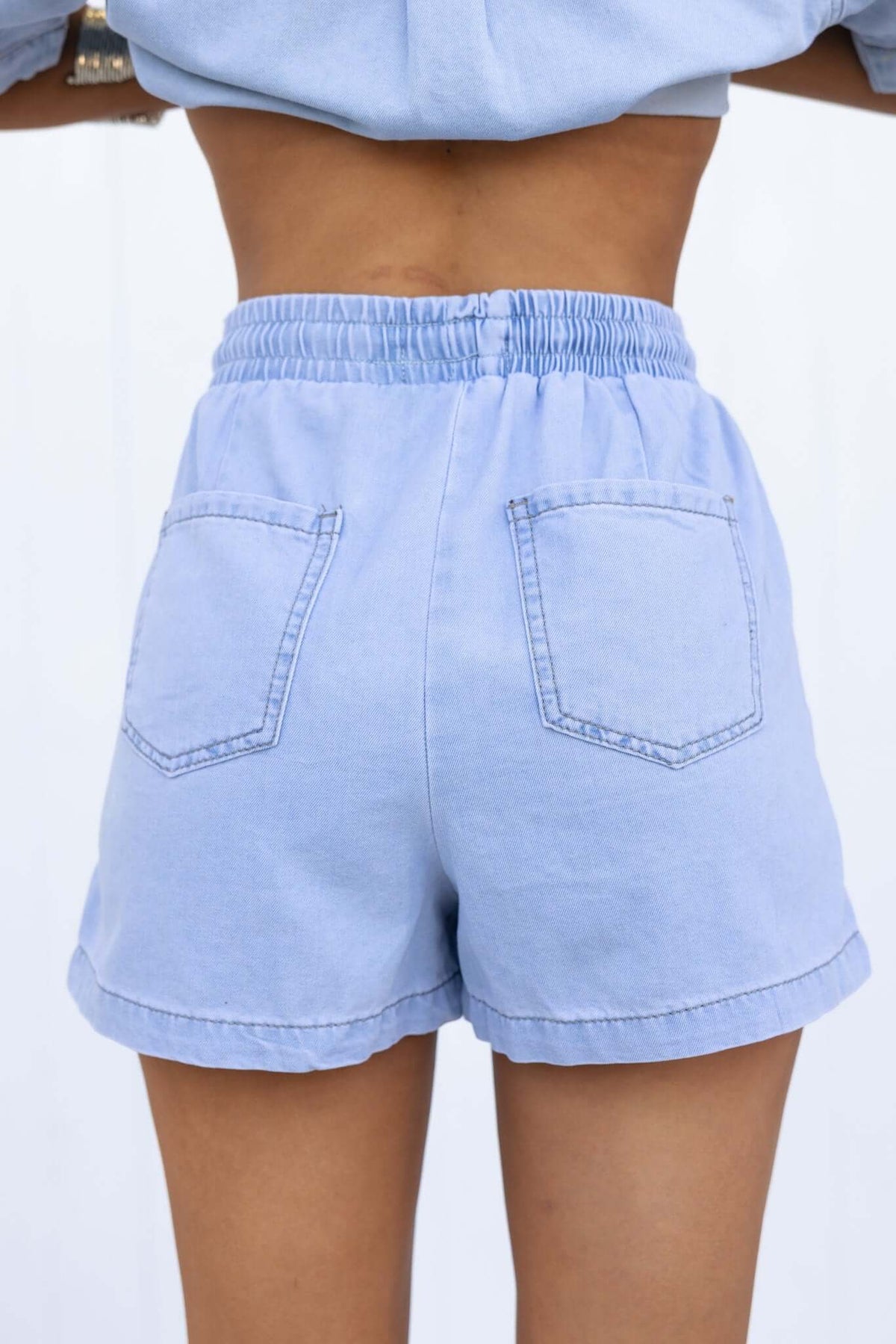 Back view of Winslow shorts, featuring elastic waist, drawstring, and chambray fabric in light blue.