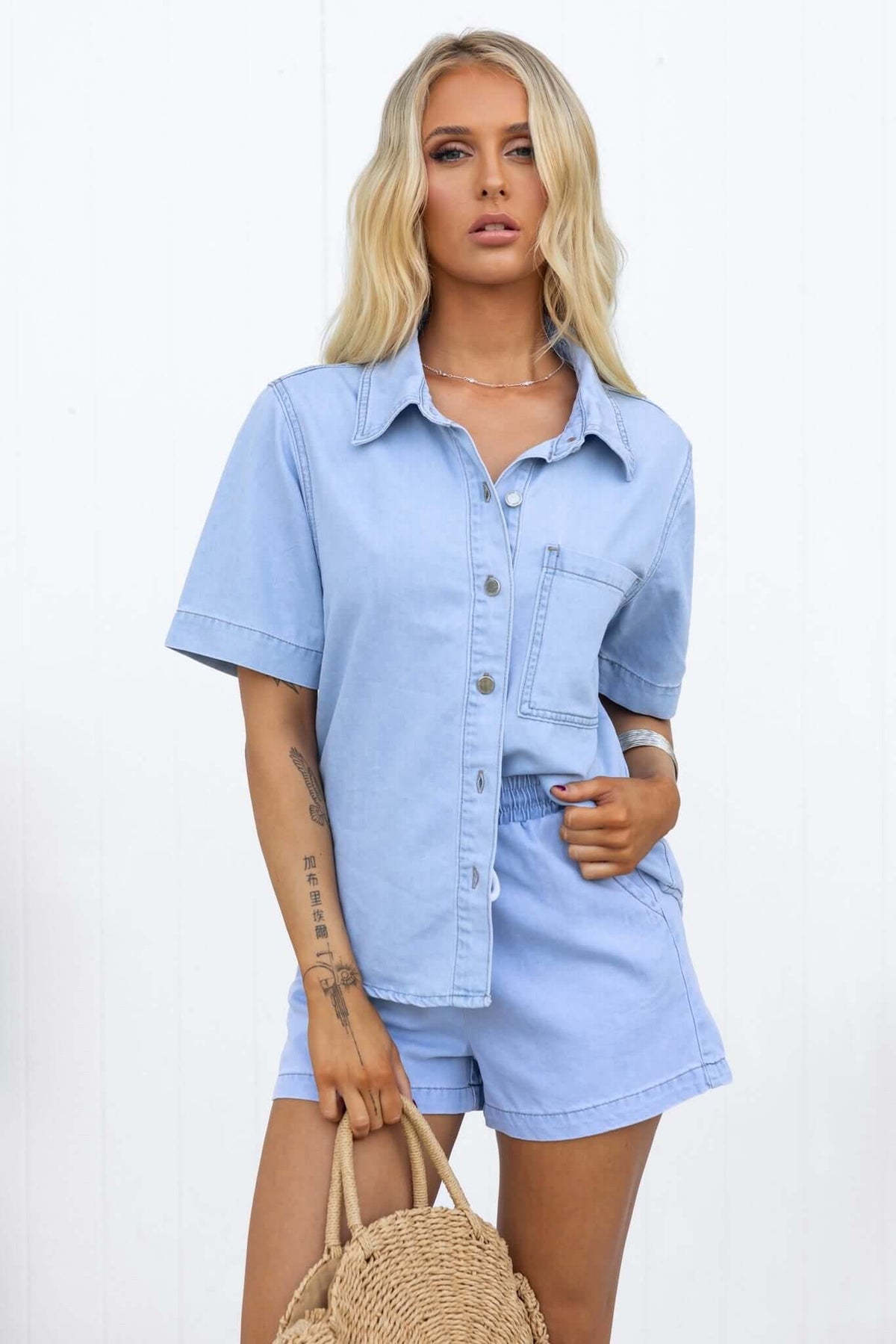 Woman wearing a light blue Winslow shirt with button-down front and chest pocket, styled with matching shorts.