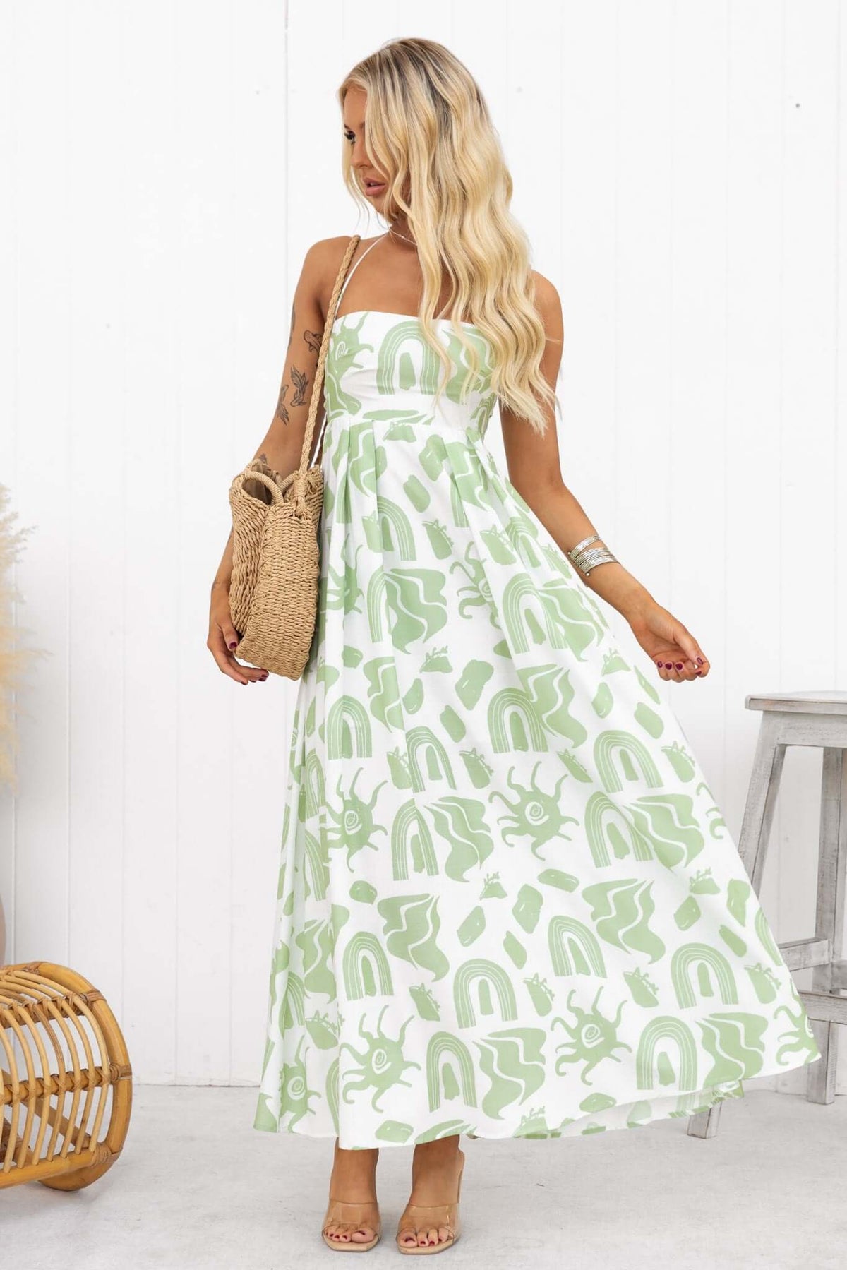 Model wearing a Derry Maxi Dress with adjustable tie straps and a square neckline, accessorized with a straw bag.