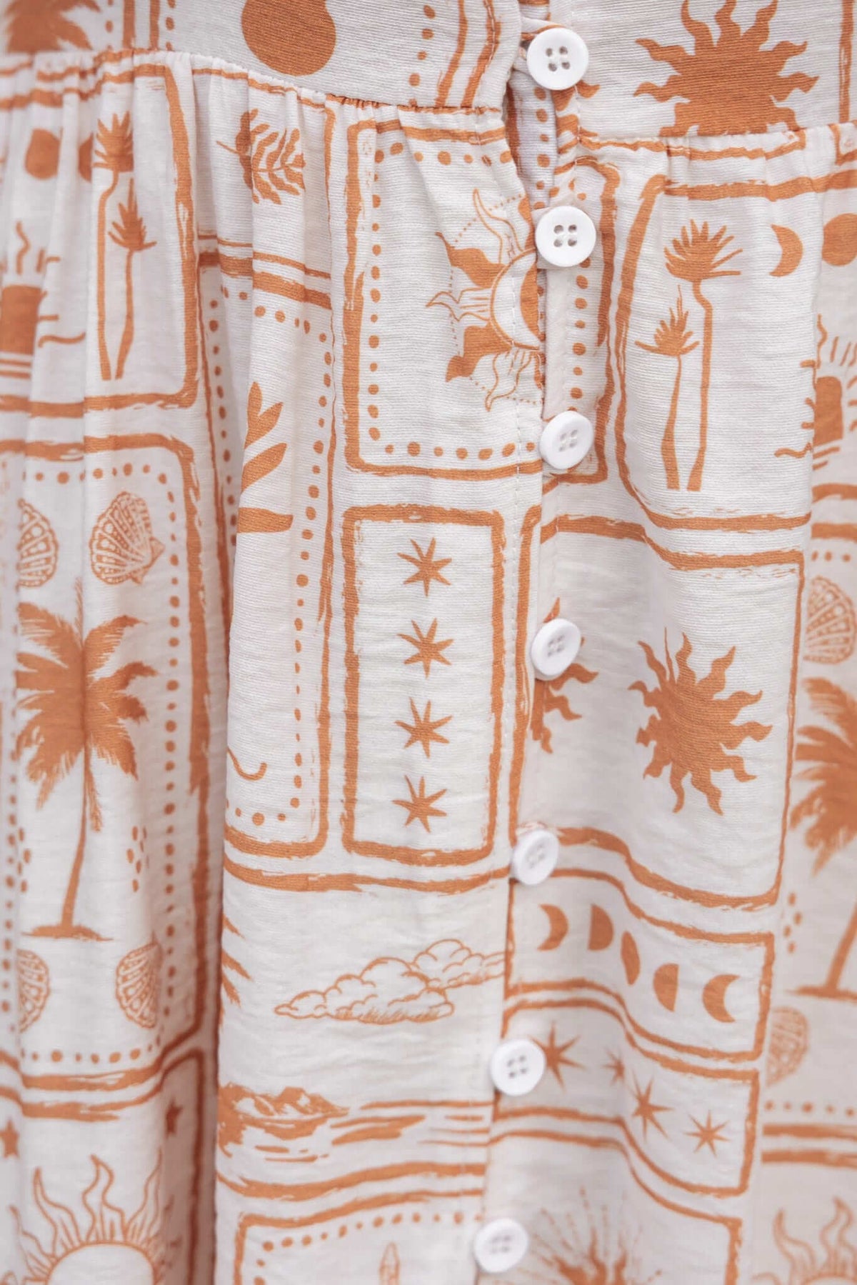 Close-up of Brekke Midi Dress fabric featuring orange palm and sun patterns with button details.