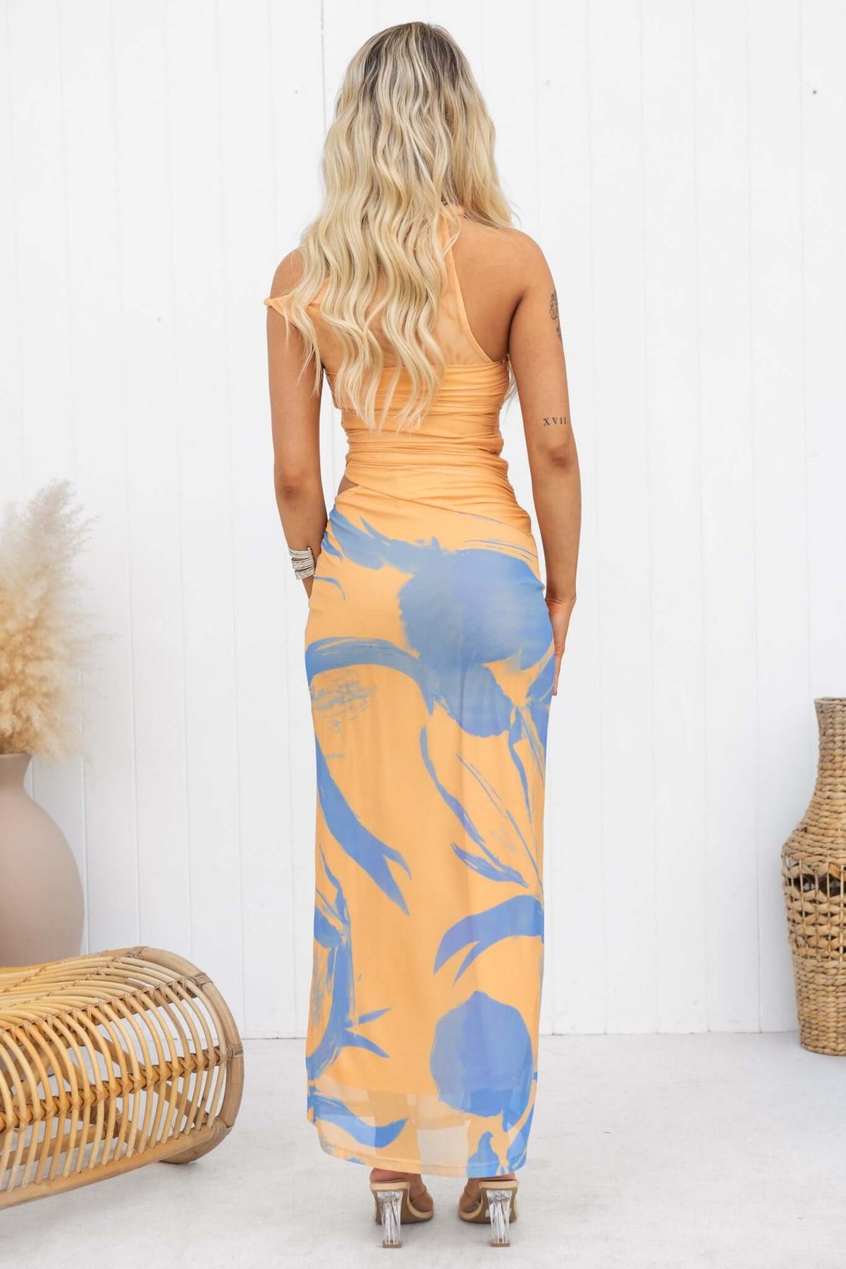 Model wearing the Ovolo Maxi Dress in orange, showcasing the cut-out side and floral print on the back view.