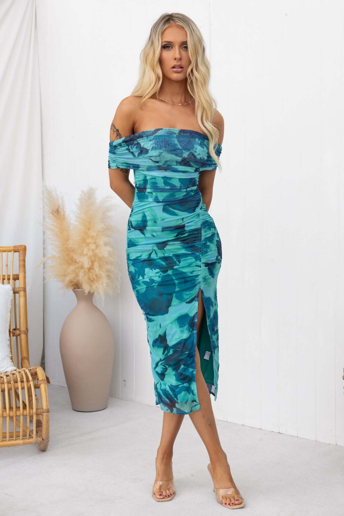 Model wearing Talinga Midi Dress with off-shoulder neckline and asymmetric hemline in teal floral design.