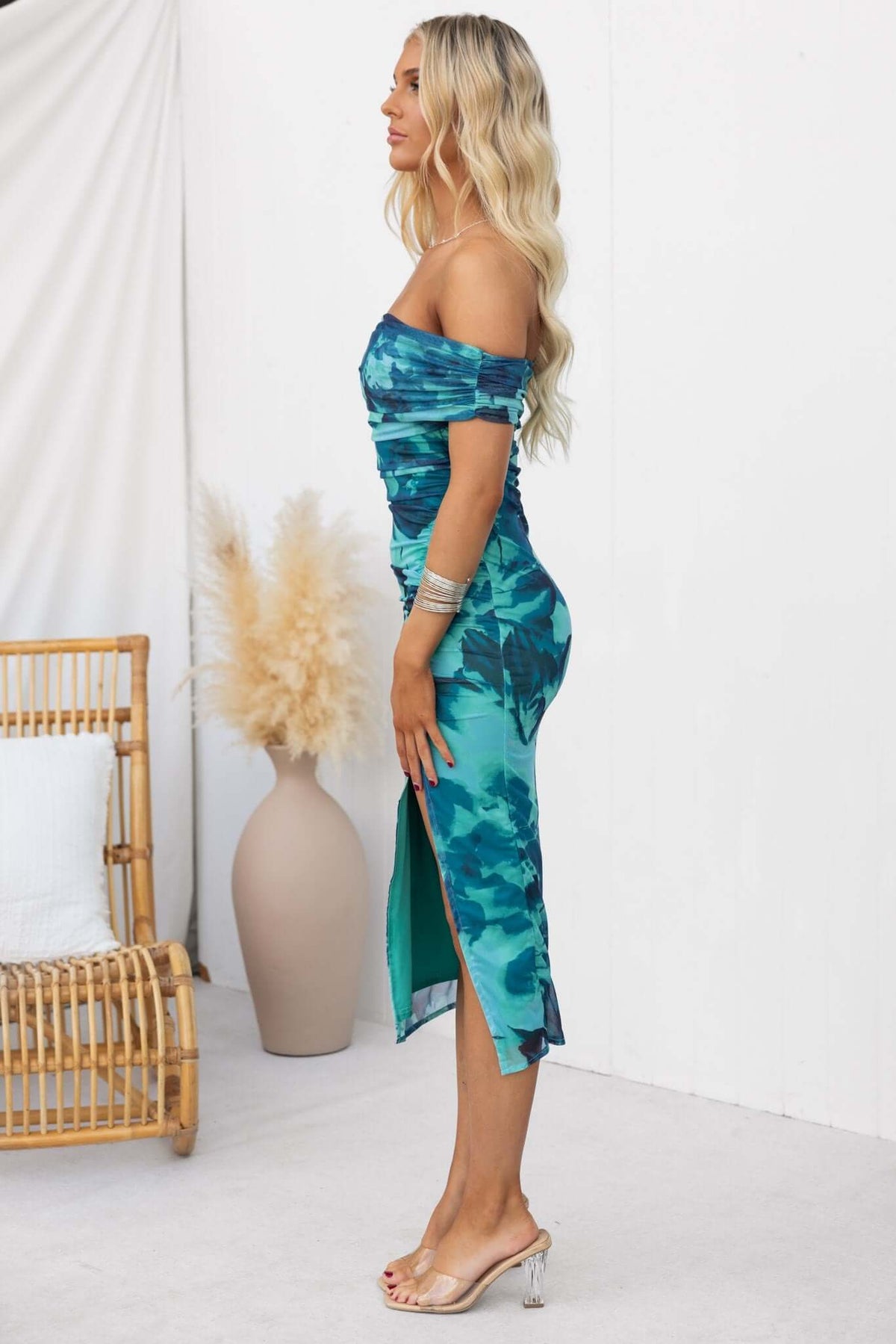 Model showcasing Talinga Midi Dress, featuring off-shoulder neckline and asymmetric hemline, styled in vibrant green hues.