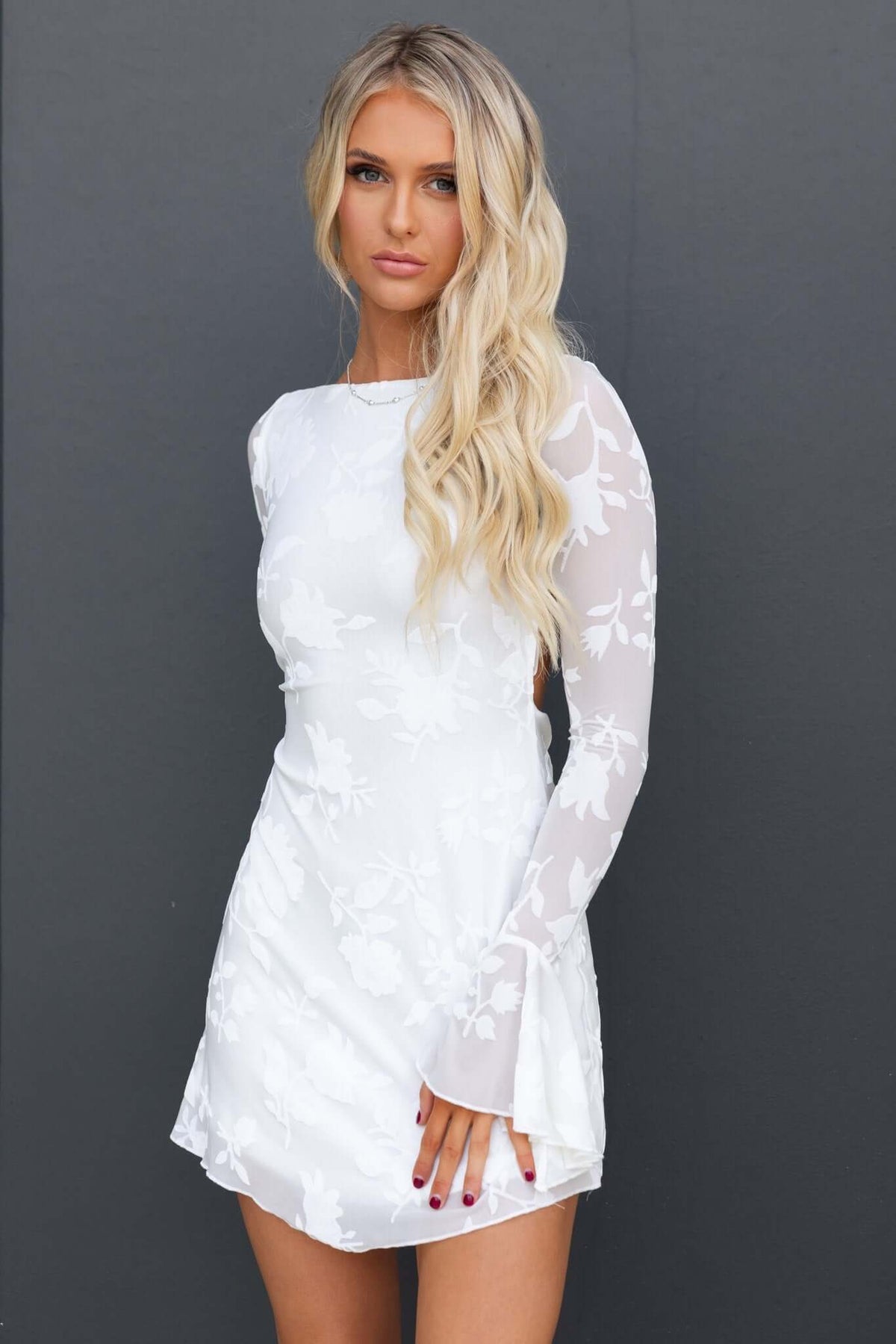 Model wearing a white Catiana Dress with long sleeves and floral embossed design, showcasing a modern and elegant look.