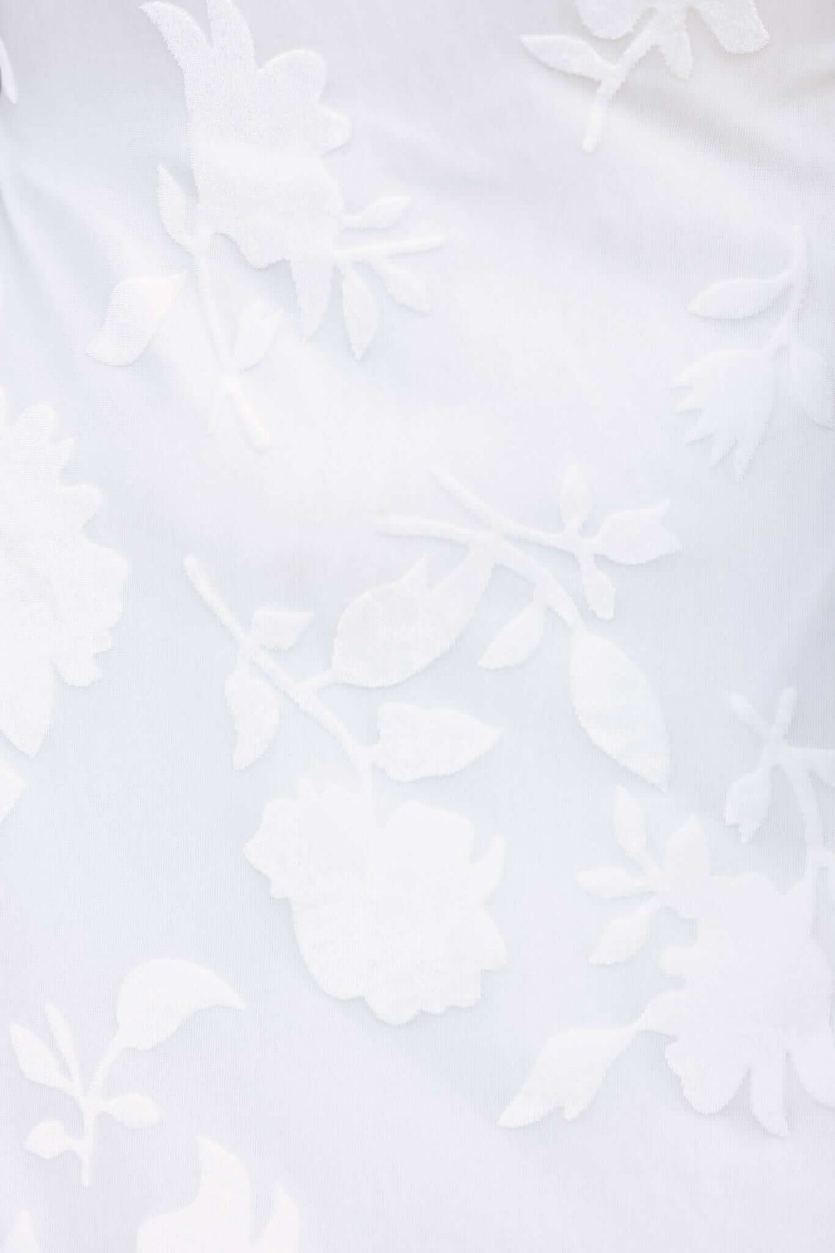 Close-up of embossed velvet print on fabric, featuring delicate white floral patterns against a soft background.