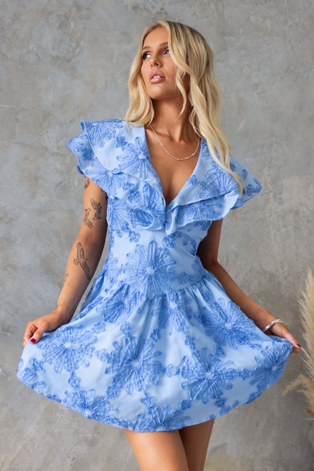 Olinda Dress in light blue with floral texture, ruffle sleeves, and a flared skirt, showcased by a model.