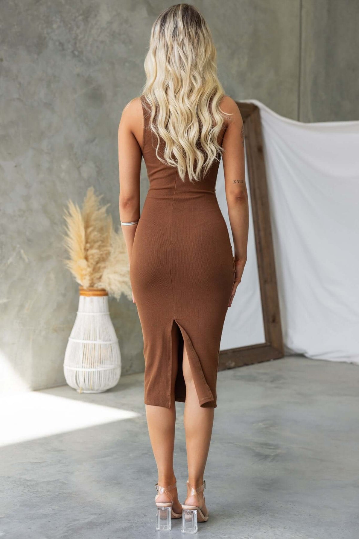 Back view of the Genna Midi Dress featuring a high neckline, button-up bust, and back split, showcased with a stylish setting.