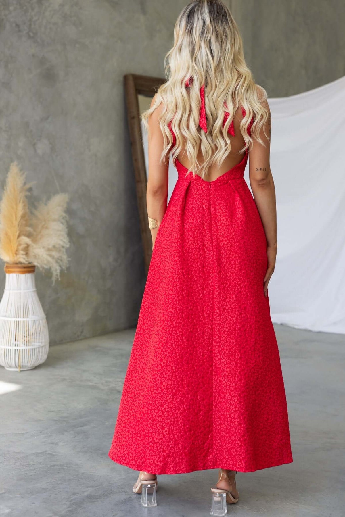 Back view of a woman in a red Ultima Maxi Dress with tie detail, showcasing textured fabric and pleated waist.