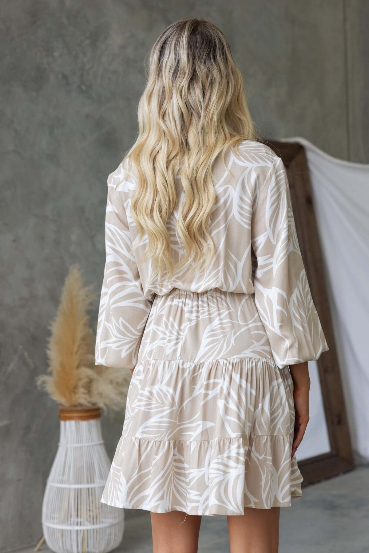 Back view of a model wearing a beige Danza dress with leaf patterns, featuring a relaxed fit and elastic waistband.