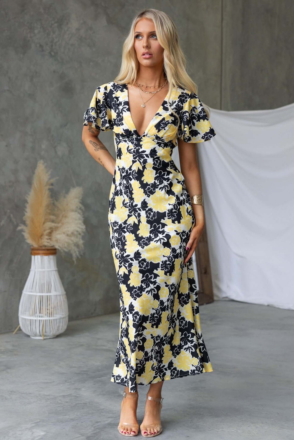 Model wearing a floral black and yellow Bartow Maxi Dress with V-neckline and flutter sleeves.