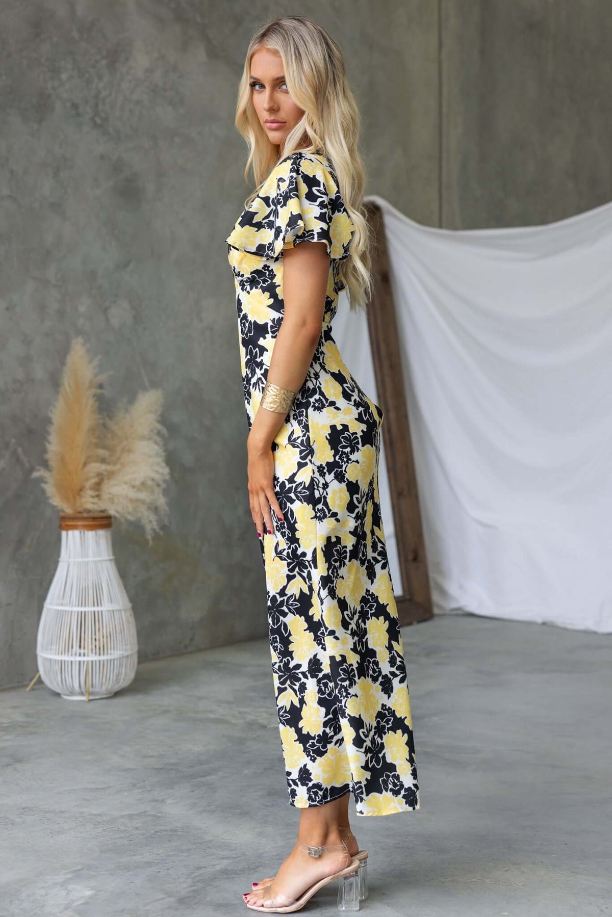 Bartow Maxi Dress in black and yellow floral pattern, featuring V-neckline and ruffle sleeves, styled elegantly in a modern setting.