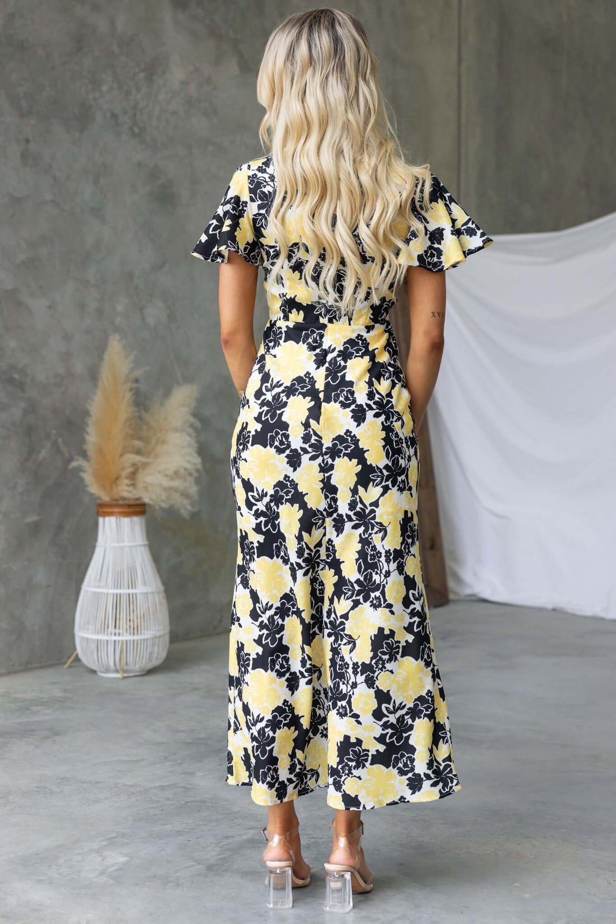 Back view of a floral maxi dress with yellow and black patterns, featuring flutter sleeves and a mid-length hem.