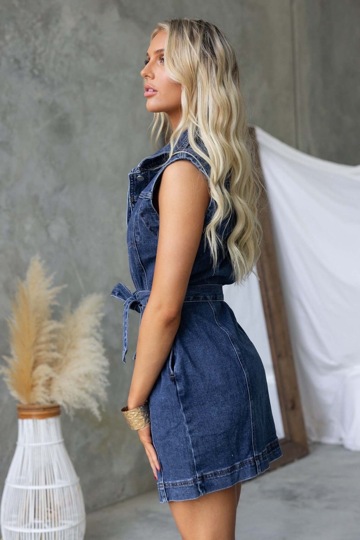 Side view of a woman in a Pokey Denim Dress with collar, button-up front, and removable belt, featuring a casual fit.