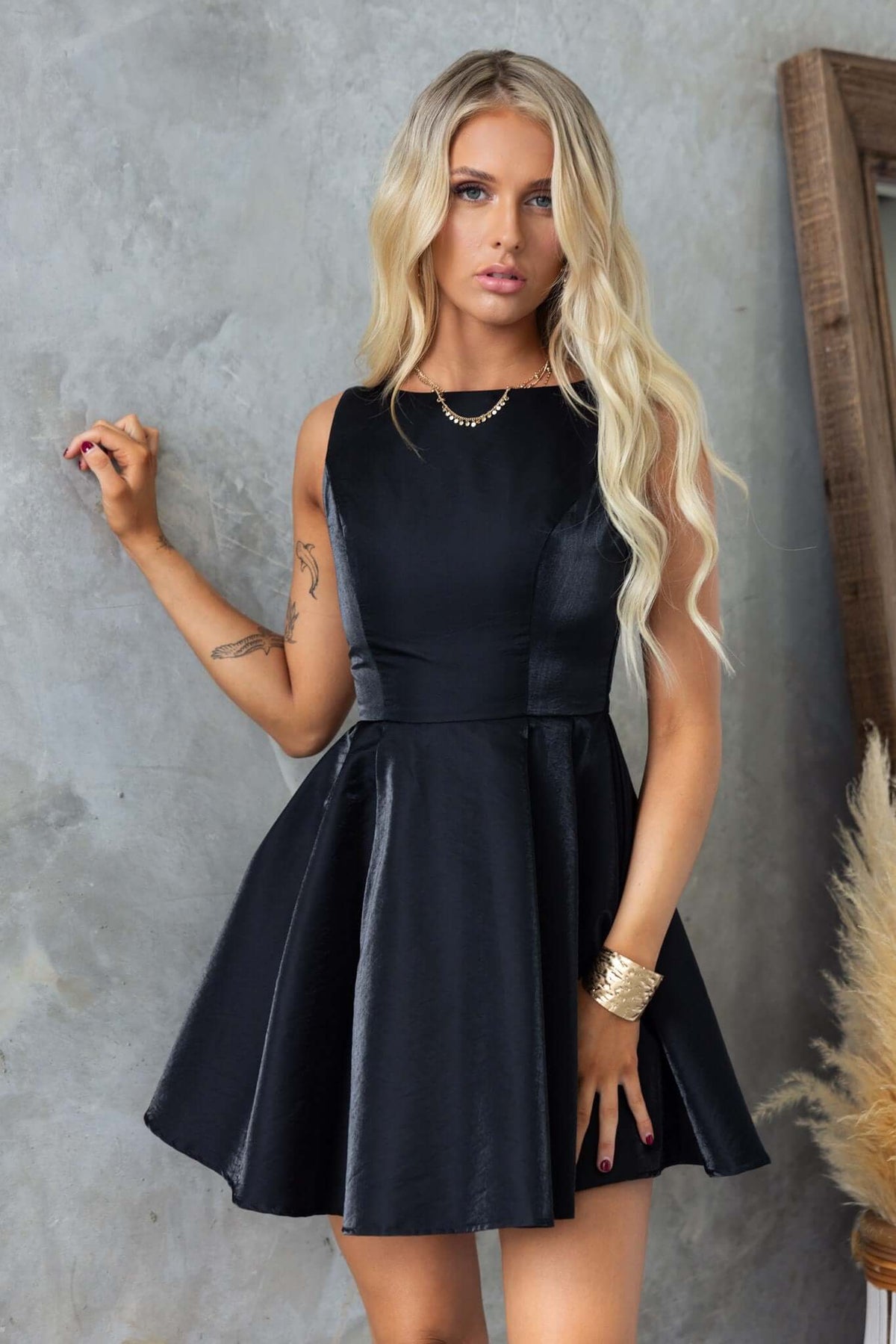 Sandy Dress featuring a high neckline, satin finish, and flared skirt, modeled by a woman against a textured backdrop.