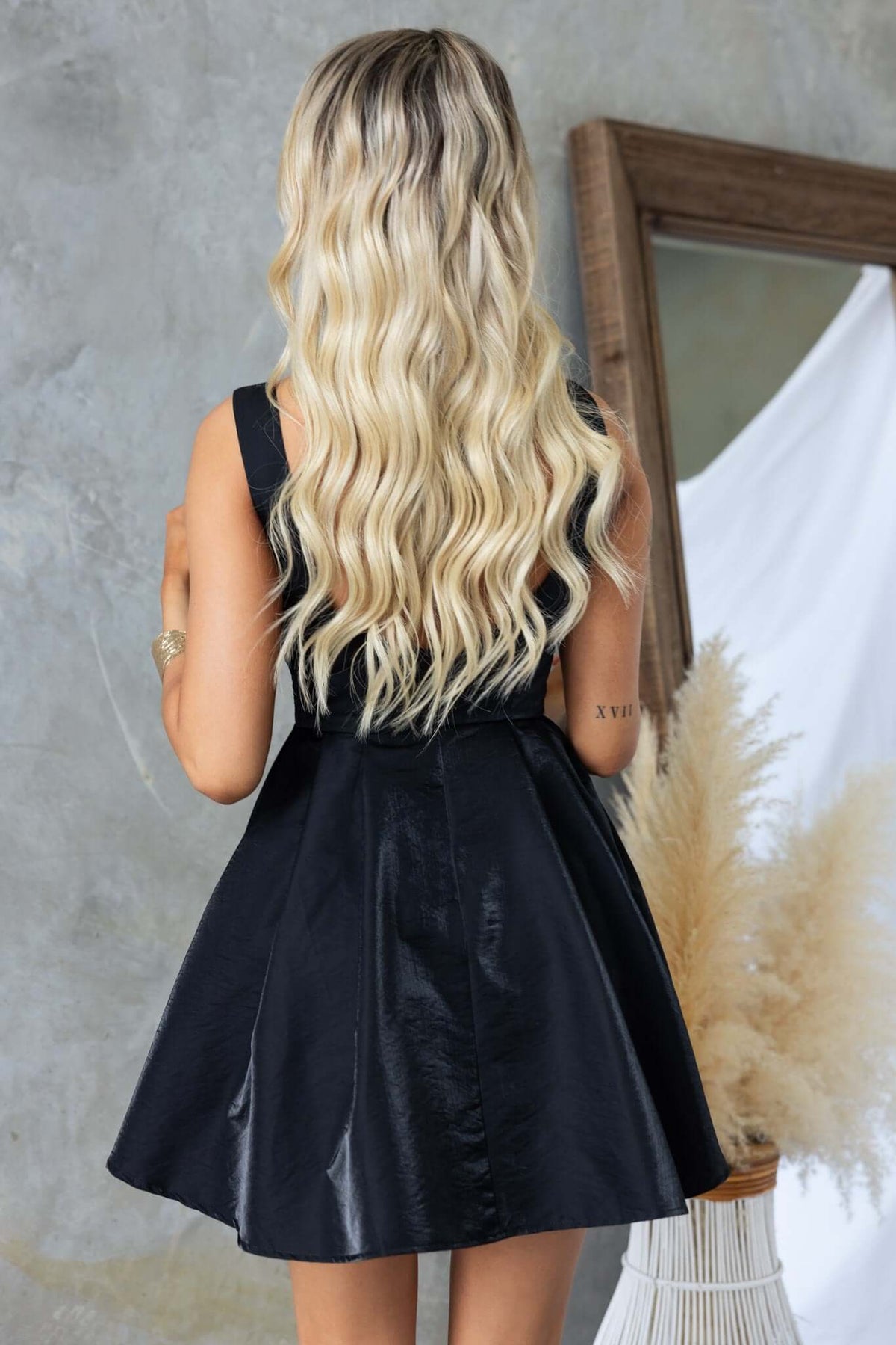 Back view of a model wearing a sleeveless black Sandy Dress with a flared skirt and long blonde hair.