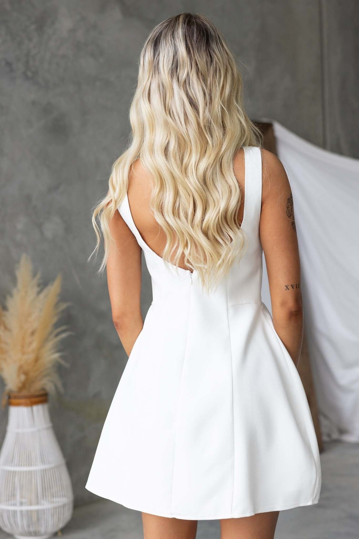 Back view of a woman wearing a white Demure Dress with scoop back and flowing skirt, styled with long wavy hair.