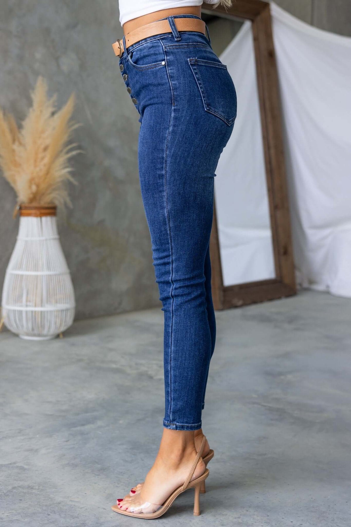 Side view of Under Cover Jeans showcasing skinny fit, mid-high waist, and button-up front, styled with clear heeled sandals.