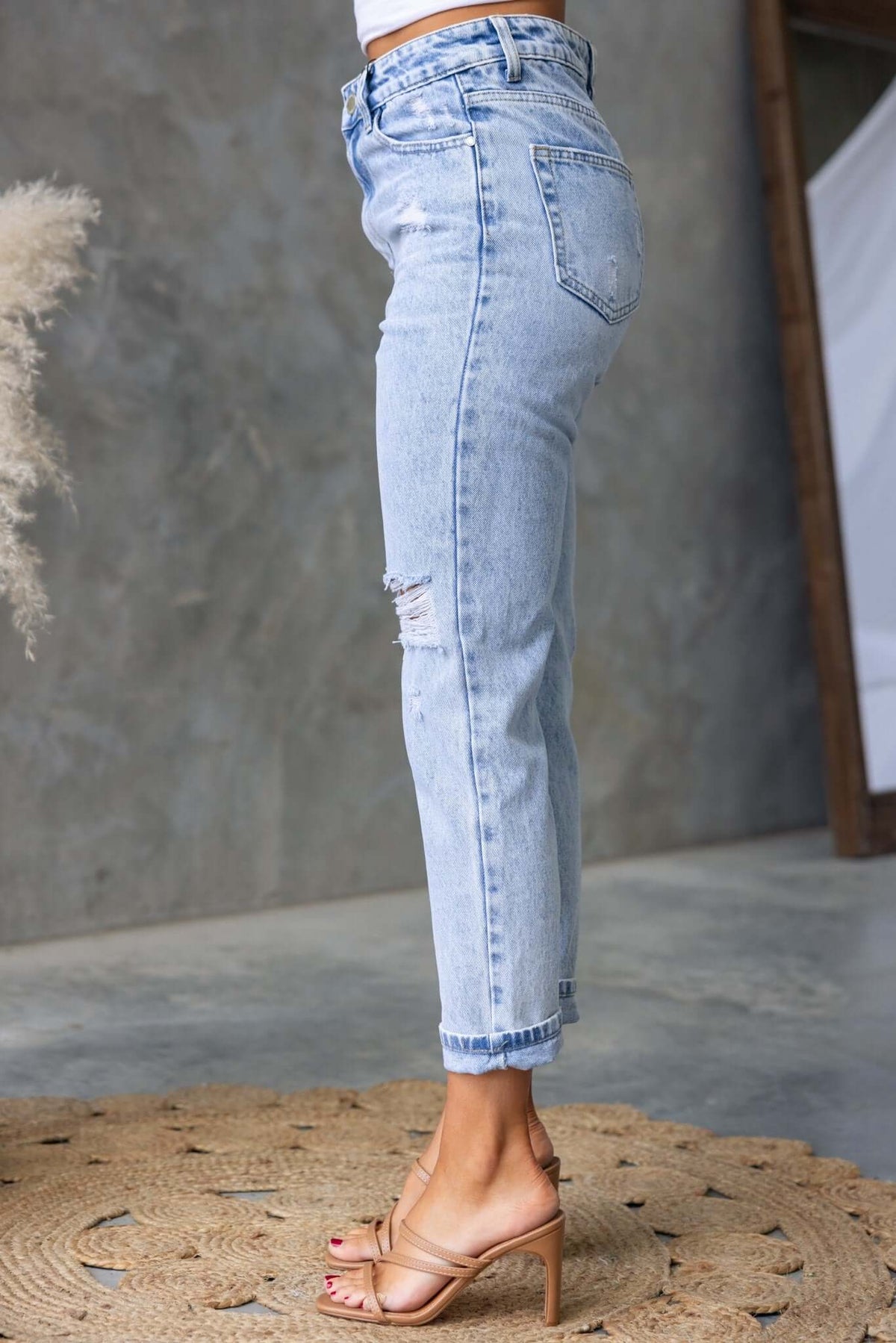 Side view of Niles Jeans, mid-high waist denim with distressed details, paired with beige heels on a circular rug.
