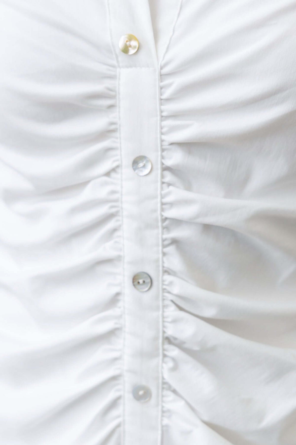 Close-up of faux button front with ruching detail on white fabric dress, showing button cuffs and textured appearance.