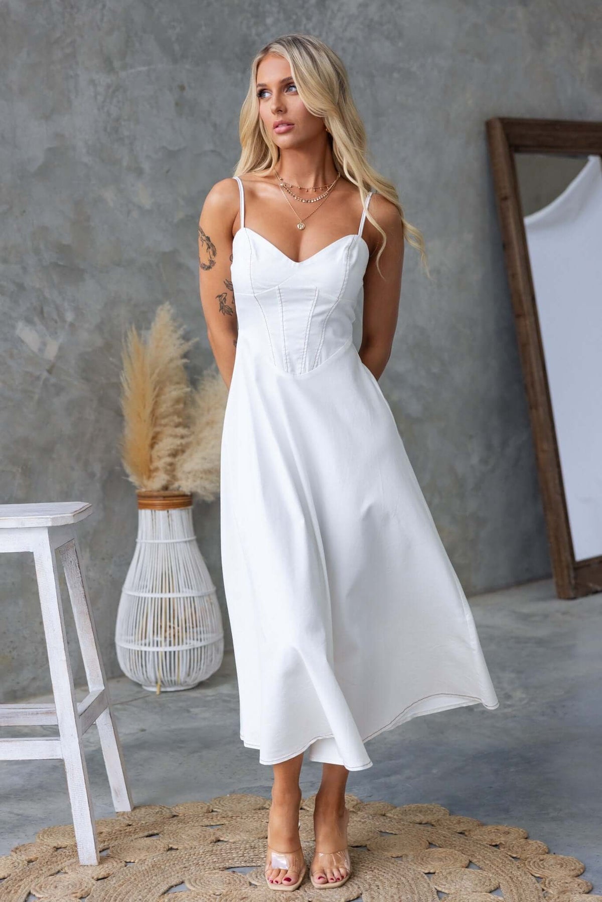Model wearing a stylish white midi dress with adjustable straps, featuring a fitted bodice and flowing skirt.
