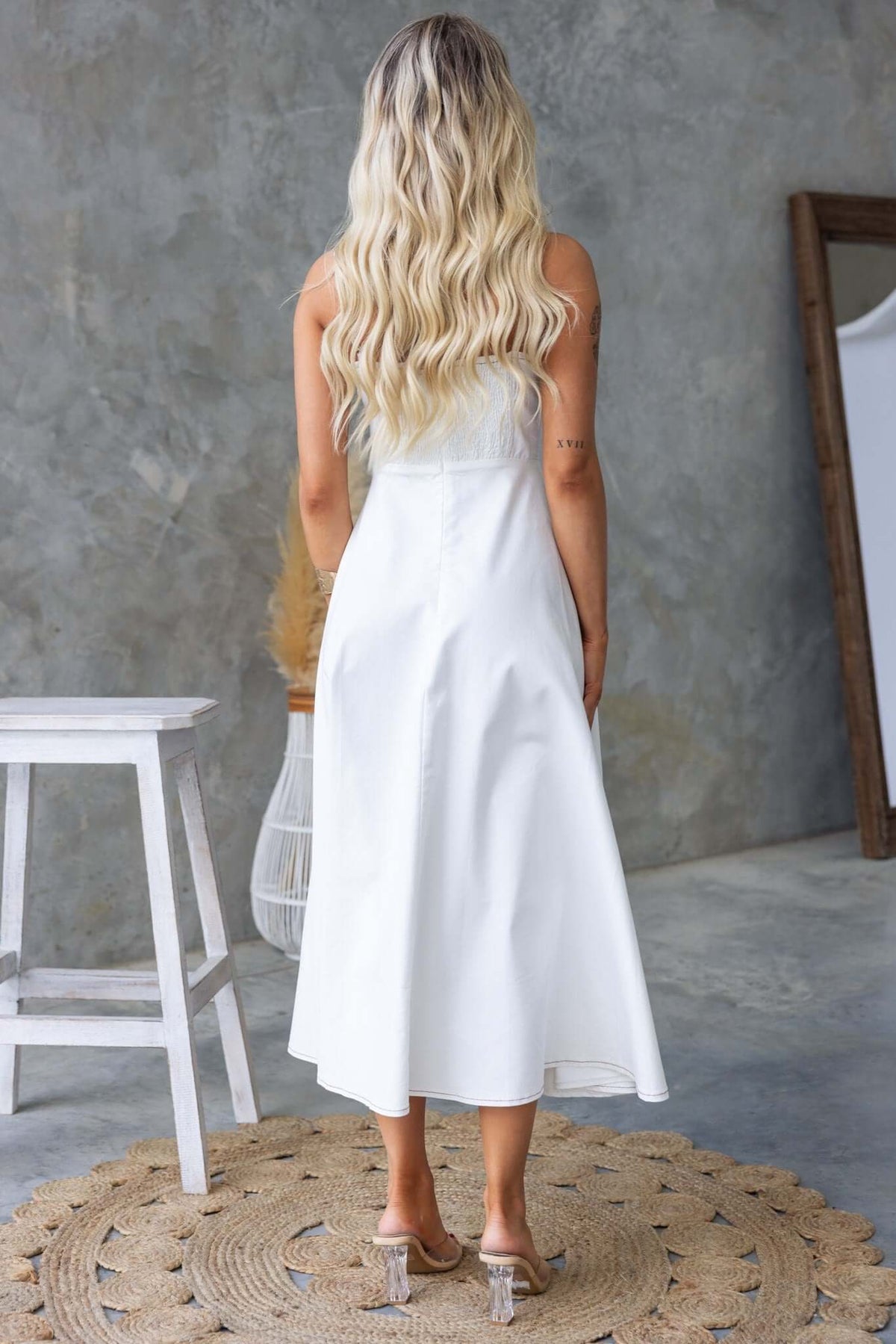 Back view of a woman in a white denim midi dress with adjustable straps, featuring a flowy design and stylish details.