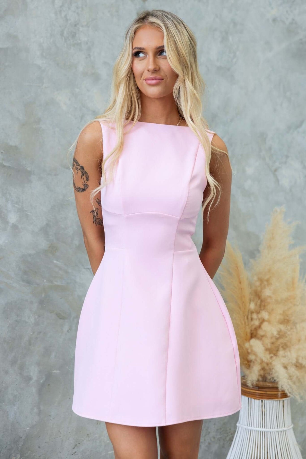 Model wearing a demure pink dress with scoop back and invisible zip, showcasing a classic and elegant style.