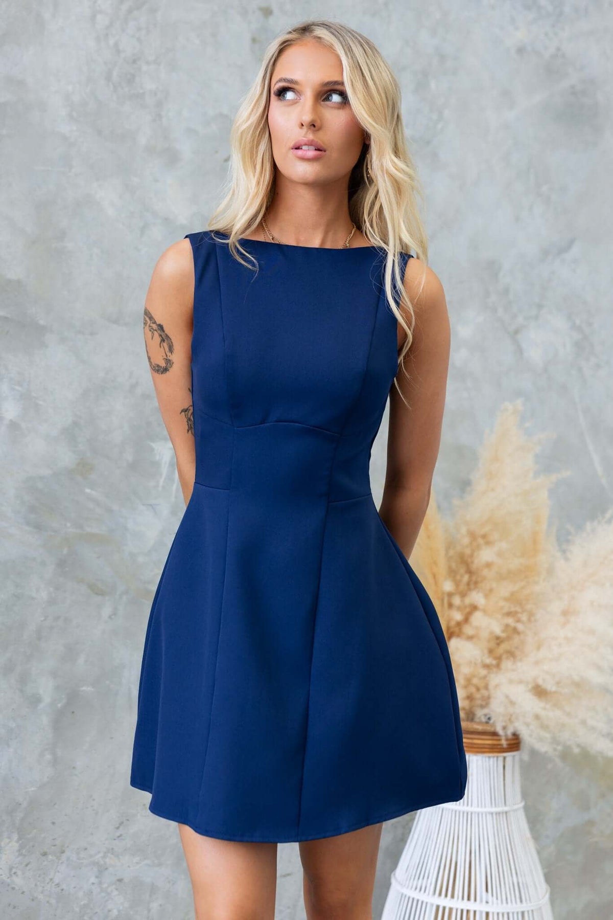 Demure dress with scoop back, invisible zip, and lined design, modeled by a woman against a textured background.
