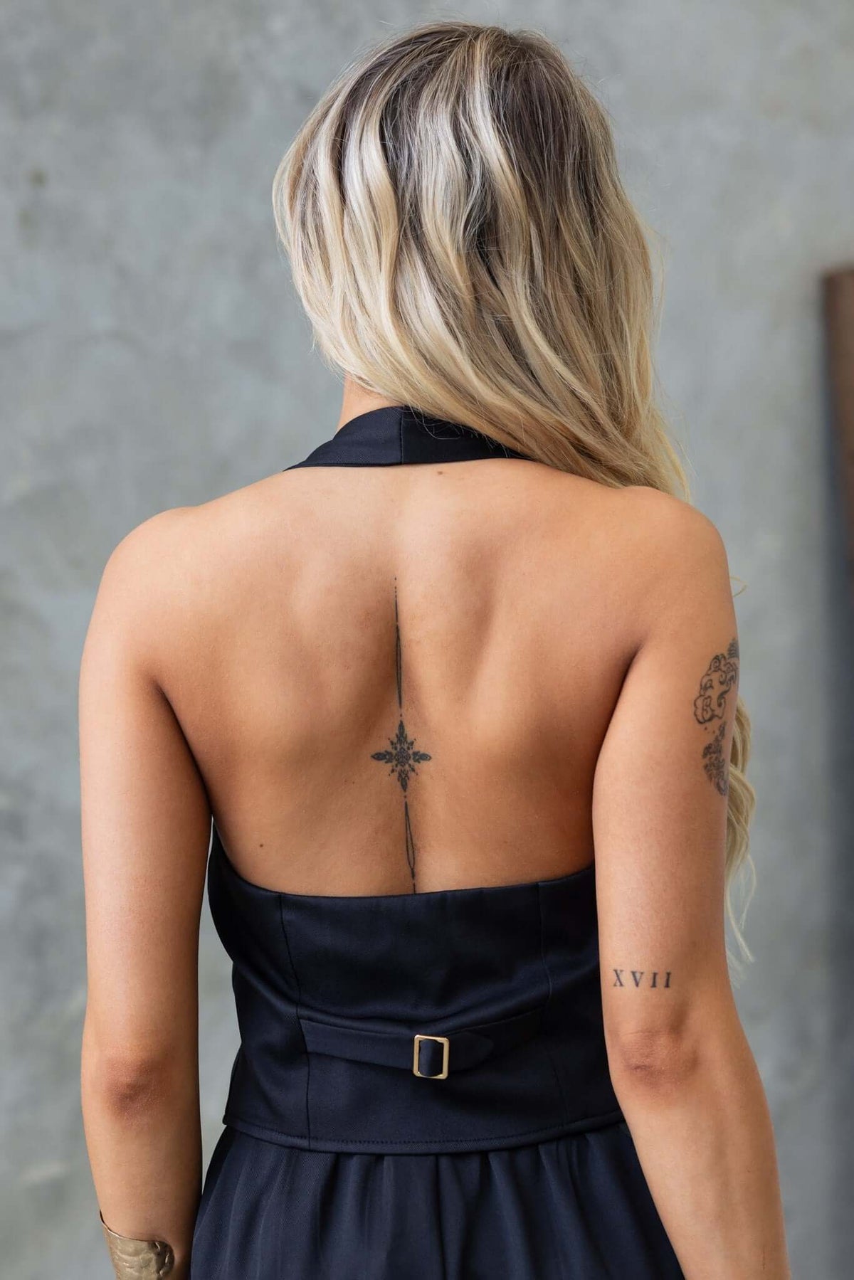 Back view of a woman in a black Lennie Top, featuring a buckle detail and a tattoo design.