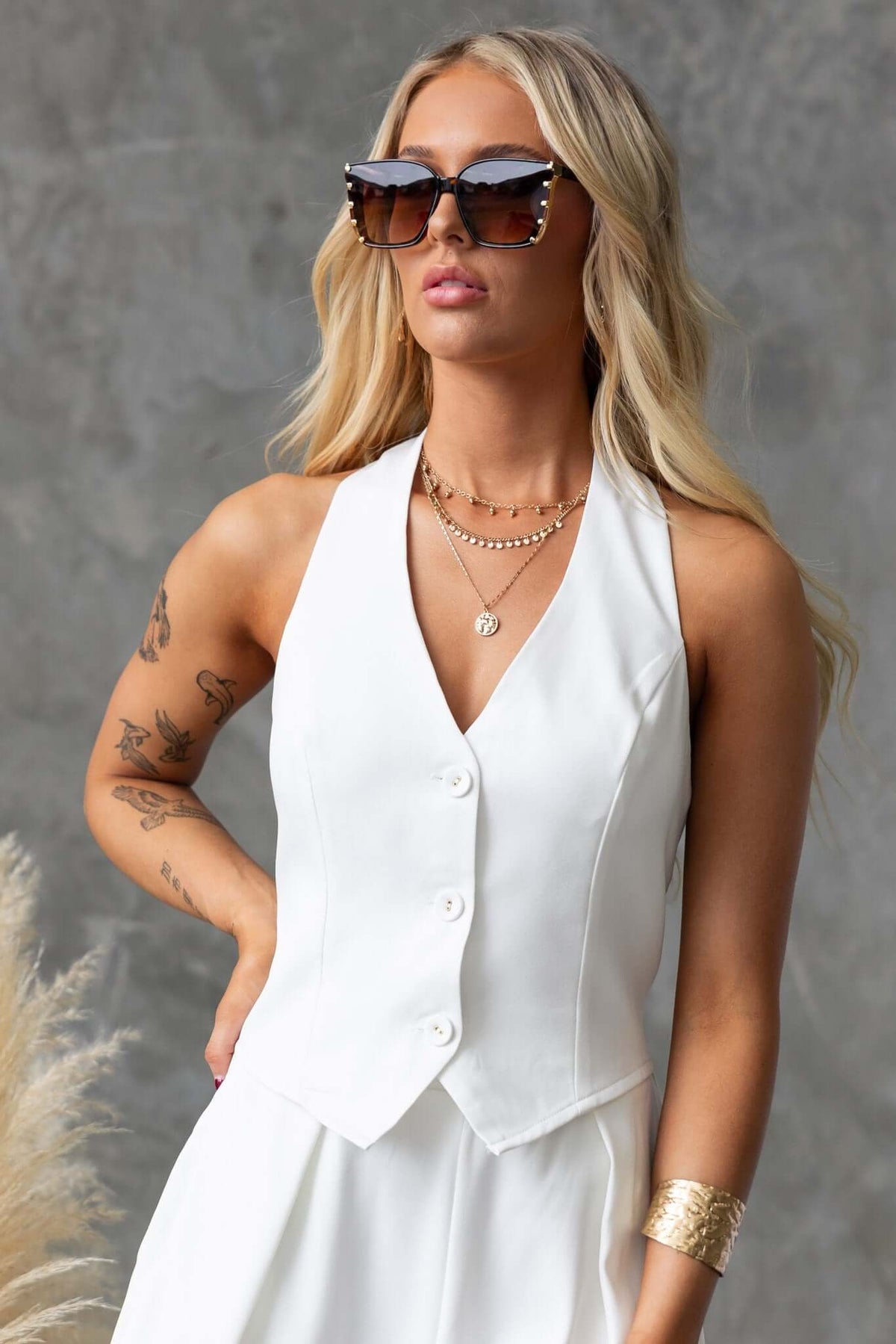 Model wearing Lennie Top, a stylish white button-down top with a halter neckline and chic sunglasses.