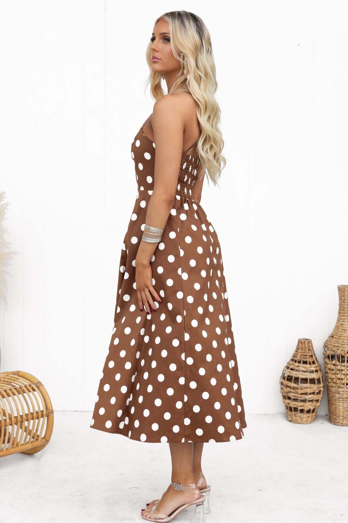 Side view of a model wearing a brown polka dot midi dress with adjustable straps and a square neckline.